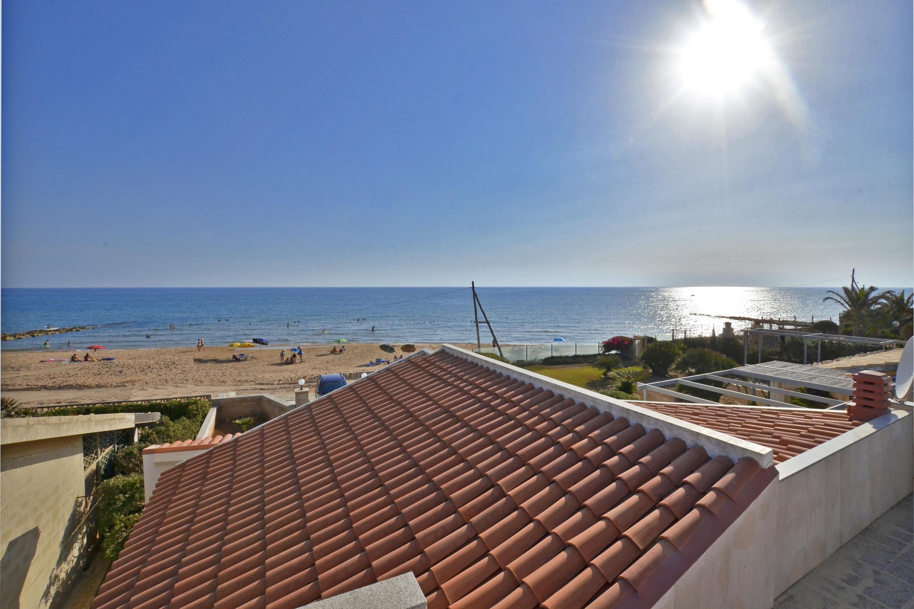 A beach view from a building with a tiled roof, a clear sky, and the ocean in the background.
