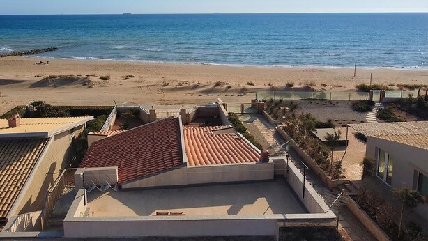 A coastal view with a beach, a clear sky, and buildings with red-tiled roofs. - Casa Apara (Scicli)