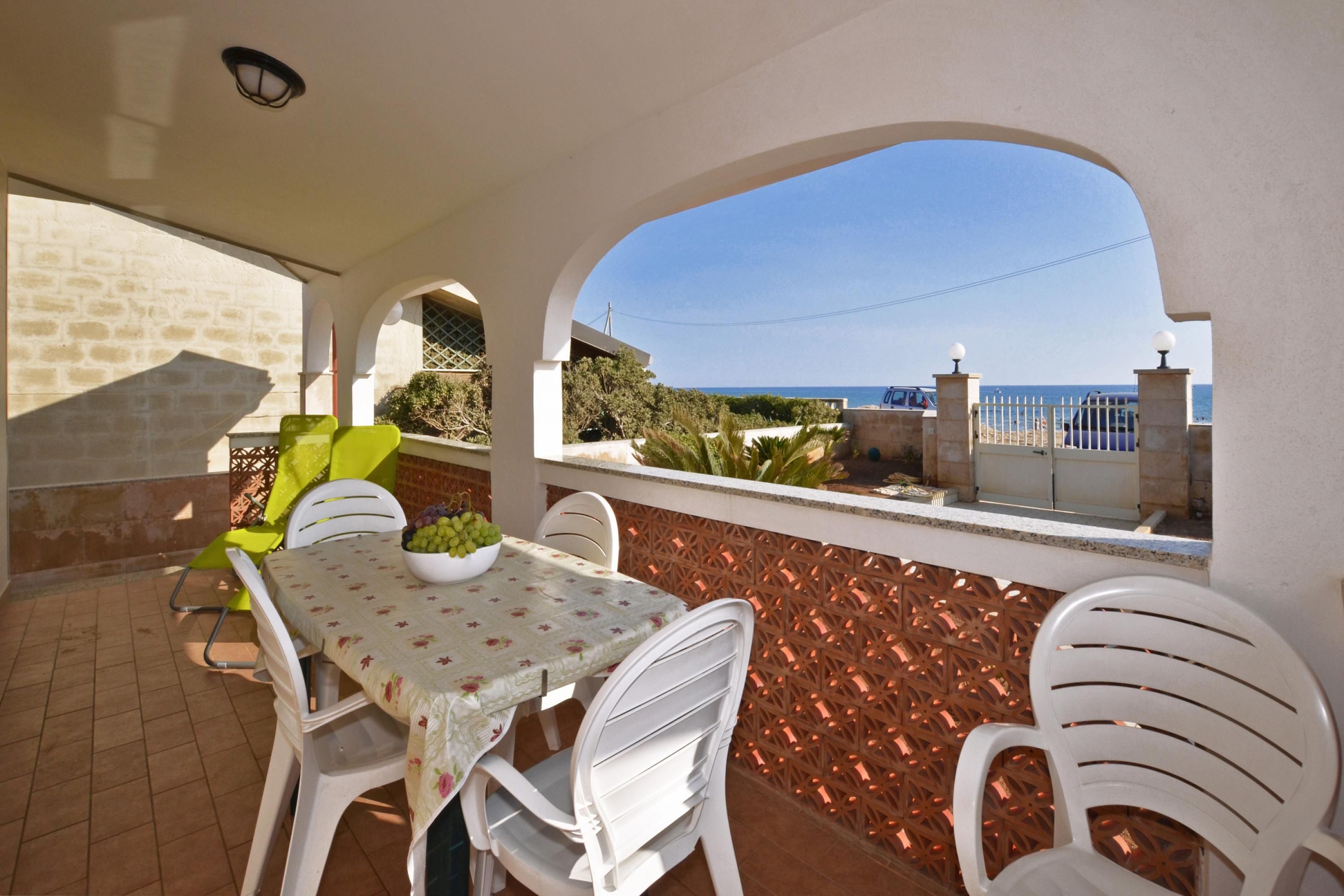 An outdoor patio with a table and chairs, a bowl of fruit, and a view of the sea.