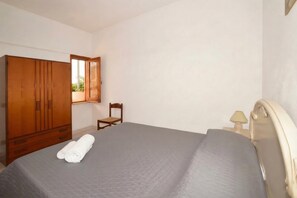 A bedroom with a bed, a wooden wardrobe, a chair, and a nightstand with a lamp. - Casa Apara (Scicli)