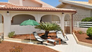 A covered patio with two lounge chairs, a table, and a green umbrella. - Casa Apara (Scicli)