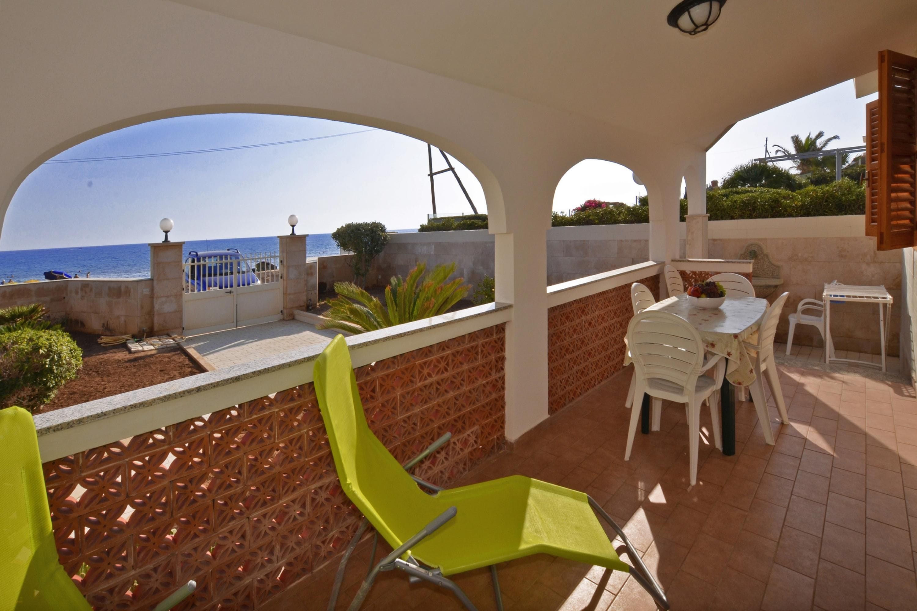 Un área de estar techada al aire libre con vistas al mar, una mesa con sillas y una valla decorativa.