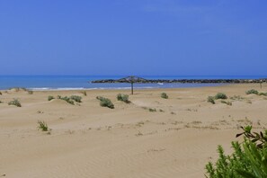 Una playa con dunas de arena, un afloramiento rocoso y una pequeña construcción.