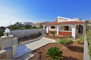 A residential property with a paved driveway, a garden with palm trees, and a white exterior with red accents. - Casa Apara (Scicli)