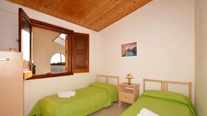 Una habitación con dos camas individuales, techo de madera, una mesita de noche con lámpara y un espejo.