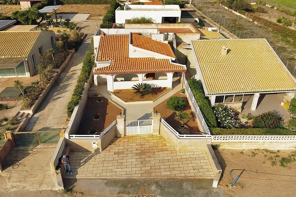 Zona residencial con una casa de techo de tejas, camino de entrada pavimentado y acceso mediante portón.