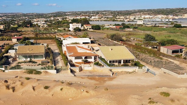 Zona residencial con casas, un primer plano arenoso y una masa de agua distante.