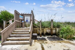 Een houten trap die leidt naar een toegangspoort tot het strand, omringd door begroeiing en waarschuwingsborden.
