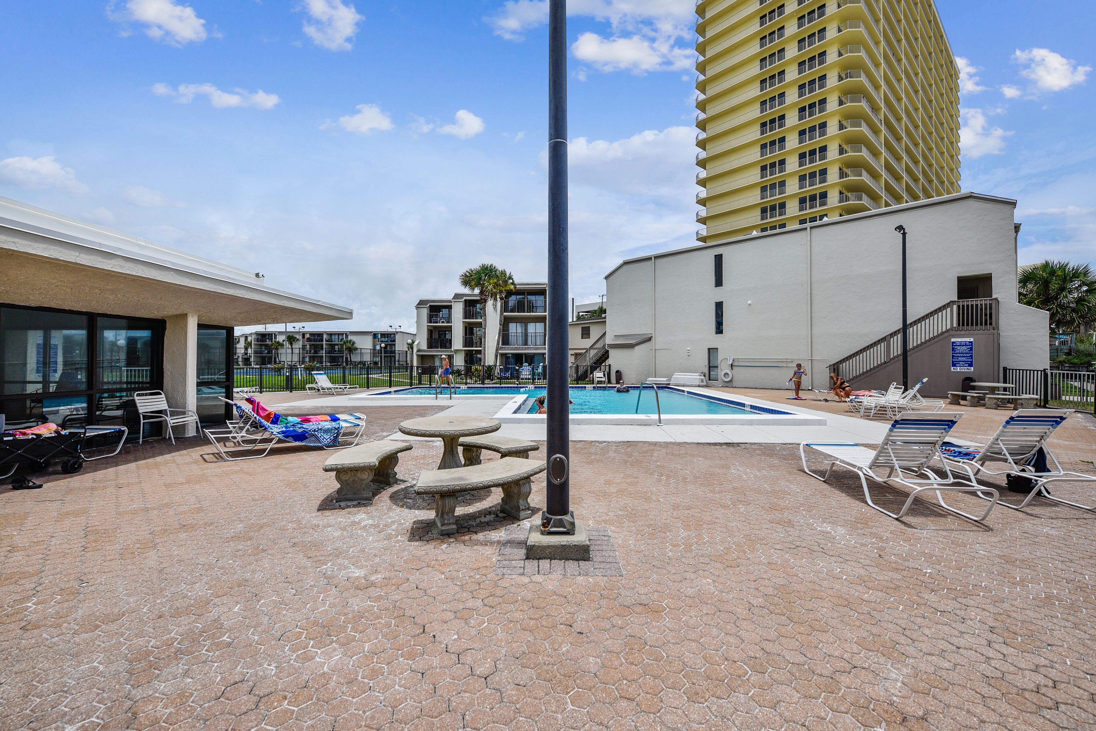 A pool area with lounge chairs, a stone table, and a tall building in the background.