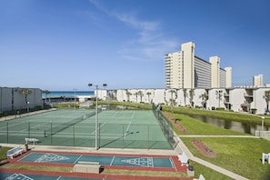 A tennis court with a pool adjacent to a hotel. - Sugar Beach by Book That Condo (Panama City Beach)