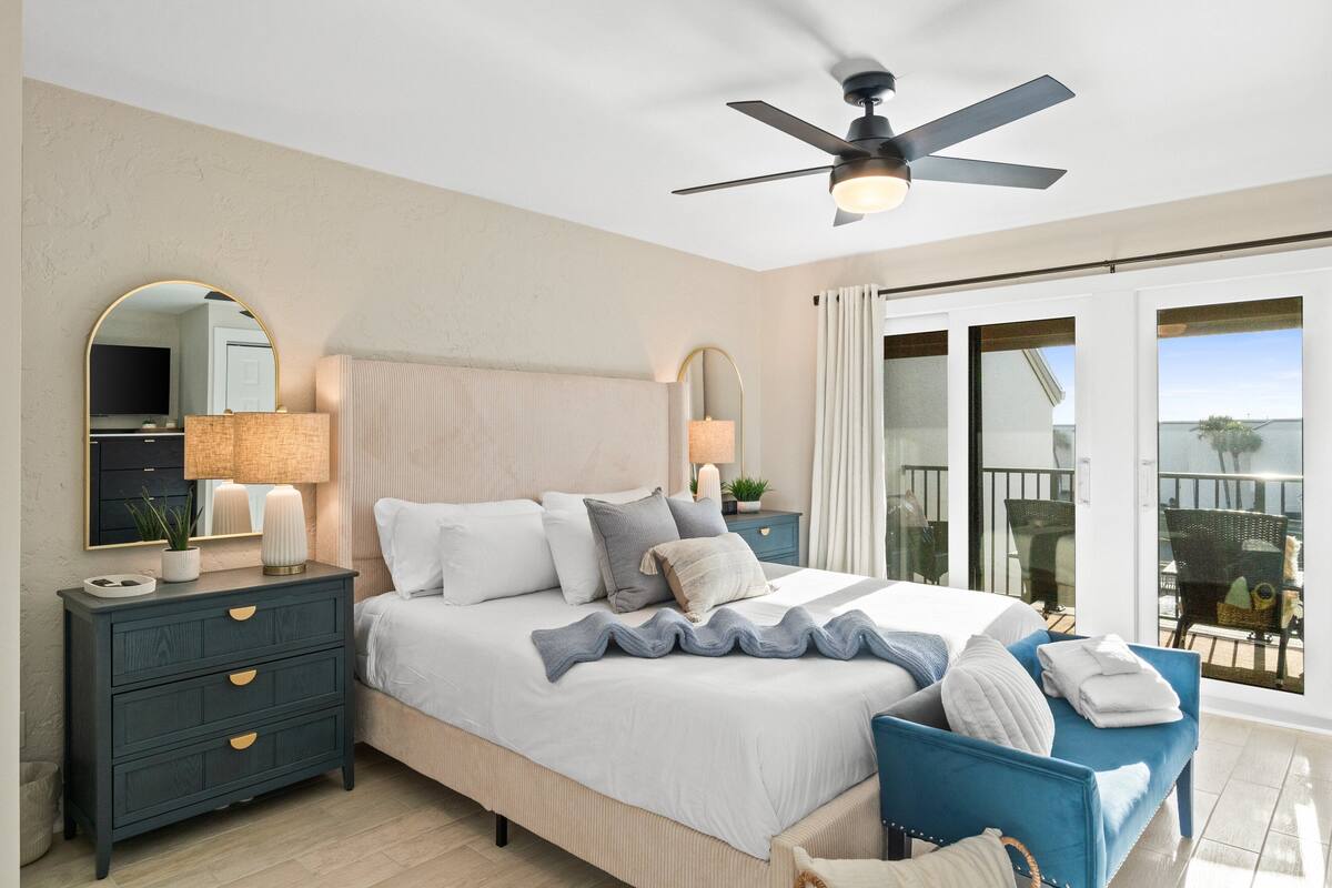 Une chambre à coucher avec un lit, des tables de chevet, un miroir et un ventilateur de plafond.