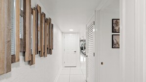 Un couloir aux murs blancs, doté d’un sol carrelé et d’une porte au fond.