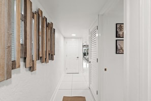 A hallway with white walls, a tiled floor, and a door at the end. - Sugar Beach by Book That Condo (Panama City Beach)