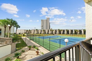 Un campo da tennis recintato, con palme e un edificio sullo sfondo.