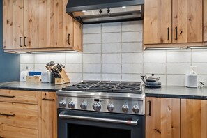 Eine moderne Küche mit Holzschränken, einem Gasherd und einer gefliesten Spritzschutzwand.