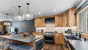 Une cuisine moderne avec des meubles en bois, un îlot central, des tabourets de bar et une grande cuisinière.