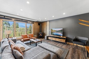 Ein modernes Wohnzimmer mit großem Fenster, Kamin, Sofa, Couchtisch und Fernseher.