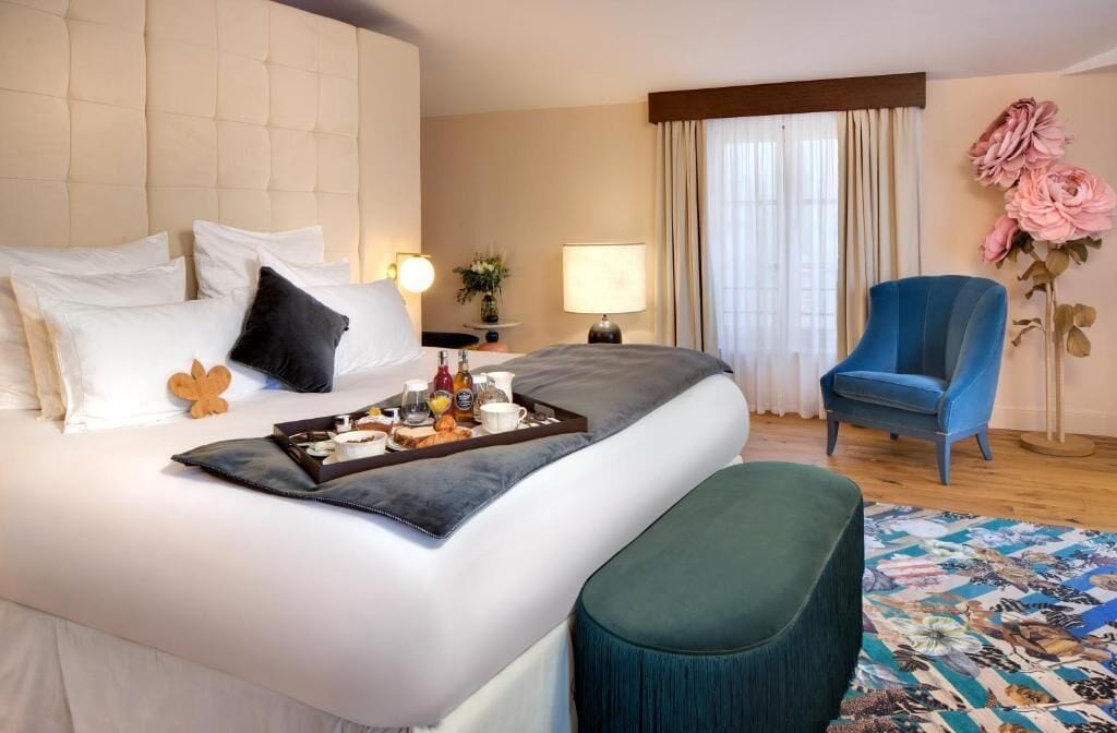 Ein Hotelzimmer mit einem großen Bett, einem Nachttisch mit Lampe, einem Sessel und einer Blumenkomposition.