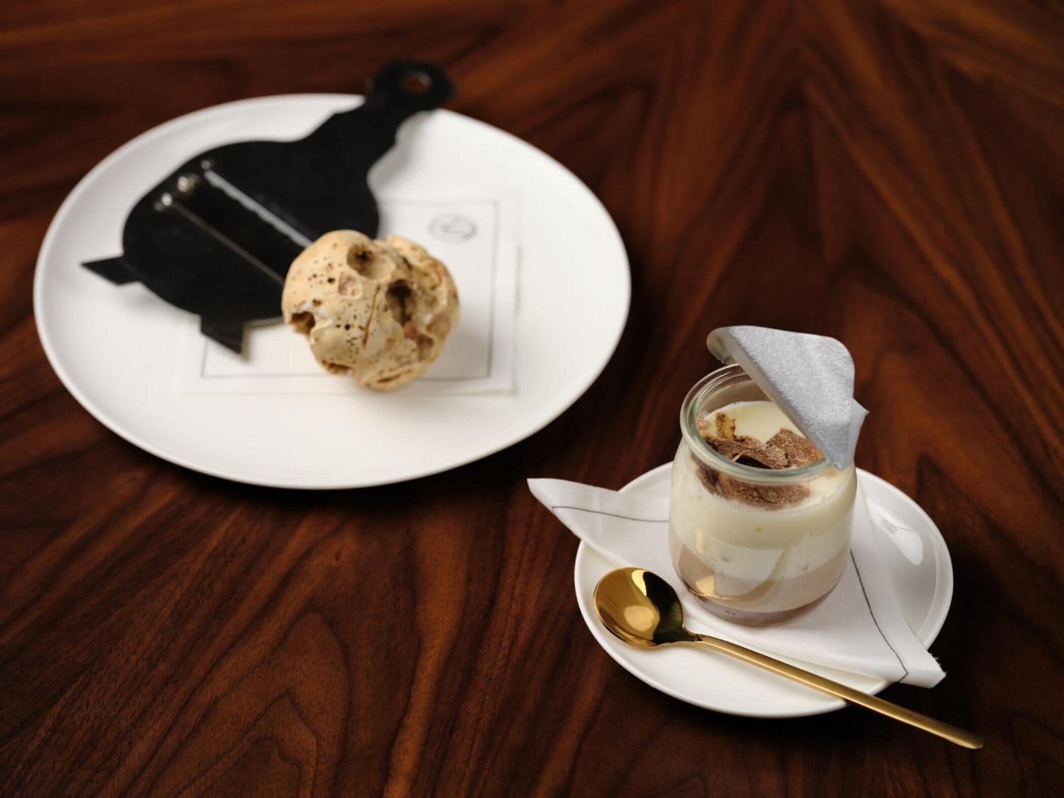 Un plato de postre con una porción de helado y un vaso de postre en capas sobre una mesa de madera.