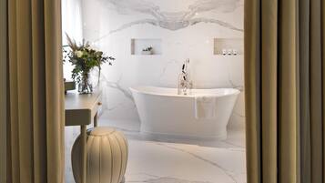 A modern bathroom with a freestanding bathtub, marble walls, and a small plant on a shelf.