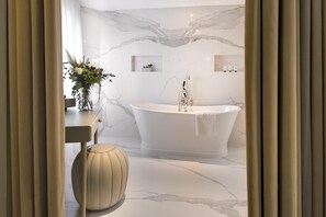 A modern bathroom with a freestanding bathtub, marble walls, and a small plant on a shelf.