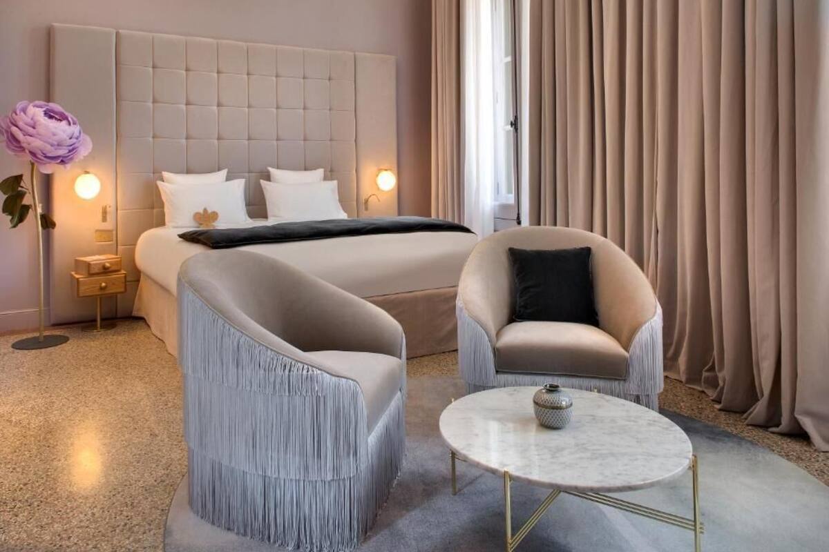 A hotel room with a large bed, two armchairs, a small table, and a nightstand with a lamp.