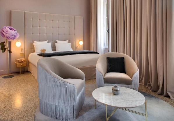 Una habitación de hotel con una cama grande, dos sillones, una mesita y una mesita de noche con lámpara.