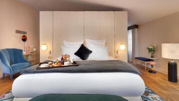 Une chambre d’hôtel avec un grand lit, un fauteuil bleu, une table de chevet sur laquelle se trouve un plateau avec divers objets, et une lampe.