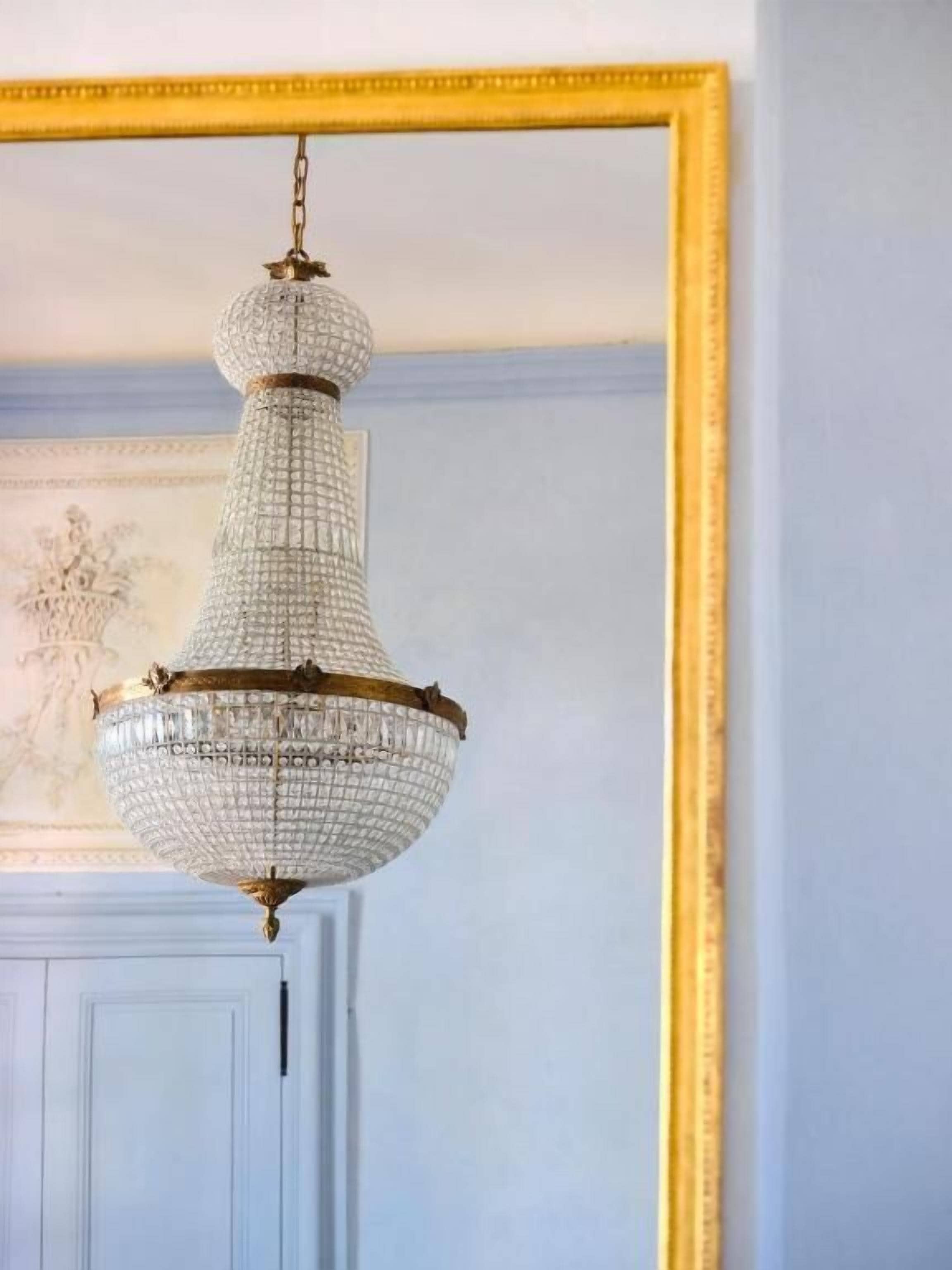A chandelier with a crystal base and gold accents, hanging from a ceiling in a room with a white door and a framed picture on the wall.