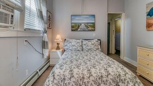 A bedroom with a bed, a nightstand, a lamp, a painting on the wall, and a dresser. - Pet Friendly 1st Floor Apt 2 Blocks to Beach & Main Ave | Private Entrance | ... (Ocean Grove)