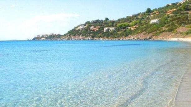 Una playa costera despejada con detalles visibles bajo el agua y una colina con edificios.