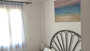 Un dormitorio con cama, un cuadro de una playa y una ventana con cortinas.
