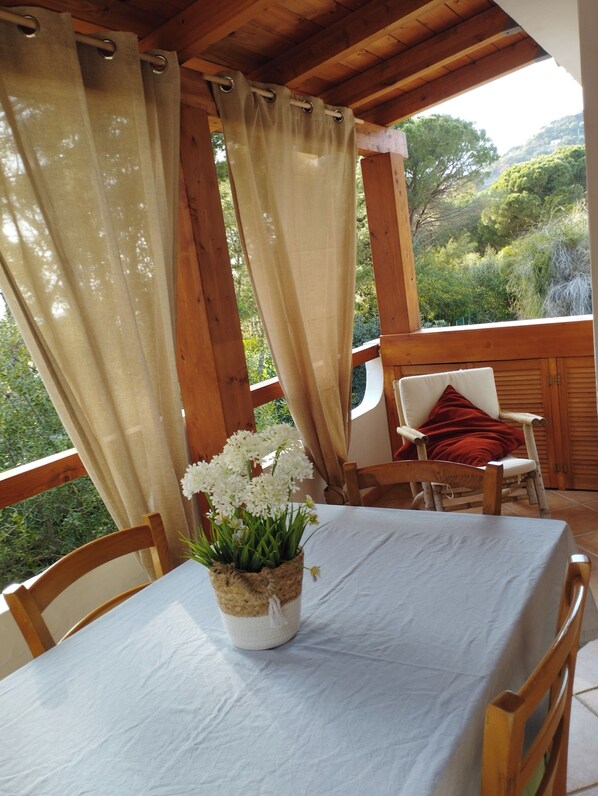 A wooden deck with a table and chairs, a potted plant, and a view of greenery.