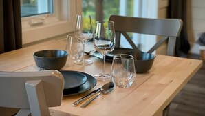 A dining table set with plates, cutlery, and wine glasses, with a view of trees through the window. - Whitecaps Cabana for Couples (Riverport)