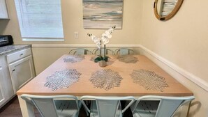A dining area with a wooden table, four chairs, a vase with white flowers, and a painting on the wall. - ★Pristine Pad ★ King Bed ★Duke ★ Long Term Stays★ (Durham)