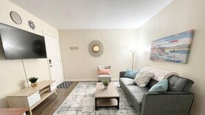 A modern living room with a grey sofa, a coffee table, a TV mounted on the wall, and a painting on the wall. - ★Pristine Pad ★ King Bed ★Duke ★ Long Term Stays★ (Durham)
