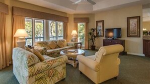 Una sala de estar con sofá, sillón, mesa de centro, televisor y ventilador de techo.