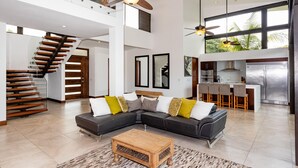 A spacious living area with a modern staircase, a sectional sofa, and a kitchen with a bar area.