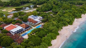 An aerial view of a coastal resort with multiple buildings, a swimming pool, and a beach.
