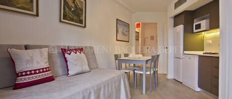 Un appartement moderne doté d’un espace de vie comprenant un canapé et une table à manger avec des chaises. Il dispose également d’une kitchenette équipée d’un four à micro-ondes et d’un réfrigérateur.