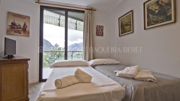A hotel room with two beds, a wooden cabinet, a television, and a large window with a view of mountains.