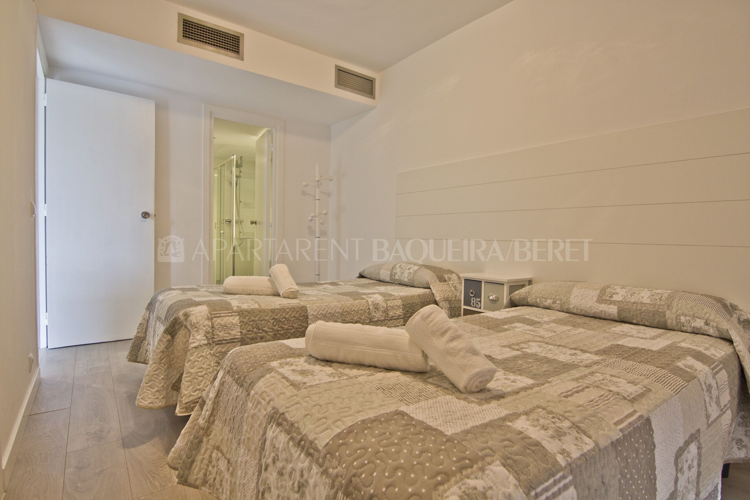 A hotel room with two beds, each with a patterned quilt and rolled towels.