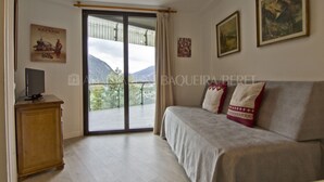 A hotel room with a bed, a television on a wooden cabinet, and a balcony with a view of mountains.