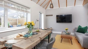 A modern living room with a wooden dining table, a sofa, and a TV mounted on the wall.