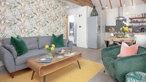 A modern living room with a grey sofa, a green armchair, and a wooden coffee table. There is a kitchen visible in the background.