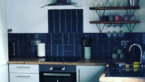 A modern kitchen with dark blue tiles, stainless steel appliances, wooden countertops, and a wooden dining table with a potted plant.