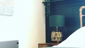 A bedroom with a bed, a bedside table with a lamp, a hanging plant, and a wall-mounted light fixture.