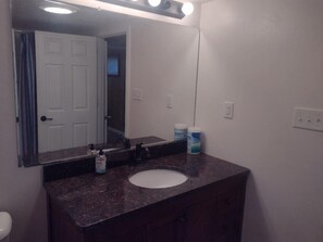 A bathroom with a white sink, dark granite countertop, and a mirror above it. There are two bottles of hand soap on the counter.