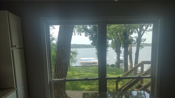 Una habitación con un amplio ventanal con vistas a un lago, una terraza de madera y un bote.