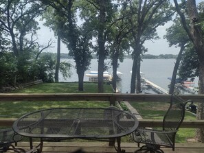 A deck with metal chairs and a table overlooking a lake, with trees and a dock in the background.